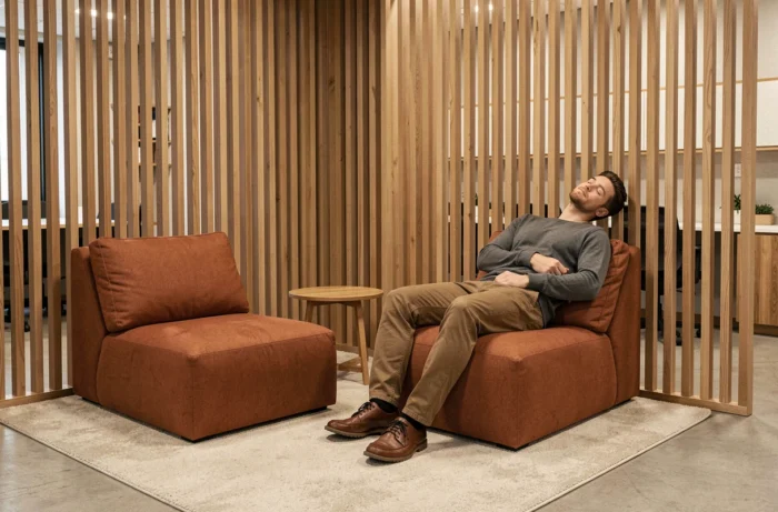 Coin calme de salle de pause avec fauteuils bas rembourrés et écran en bois ajouré pour la micro-sieste ou la détente en entreprise